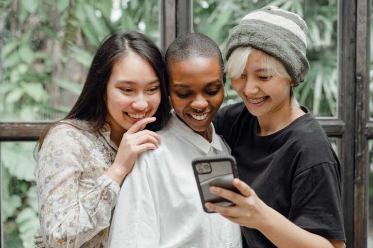Three friends laughing together while looking at a phone