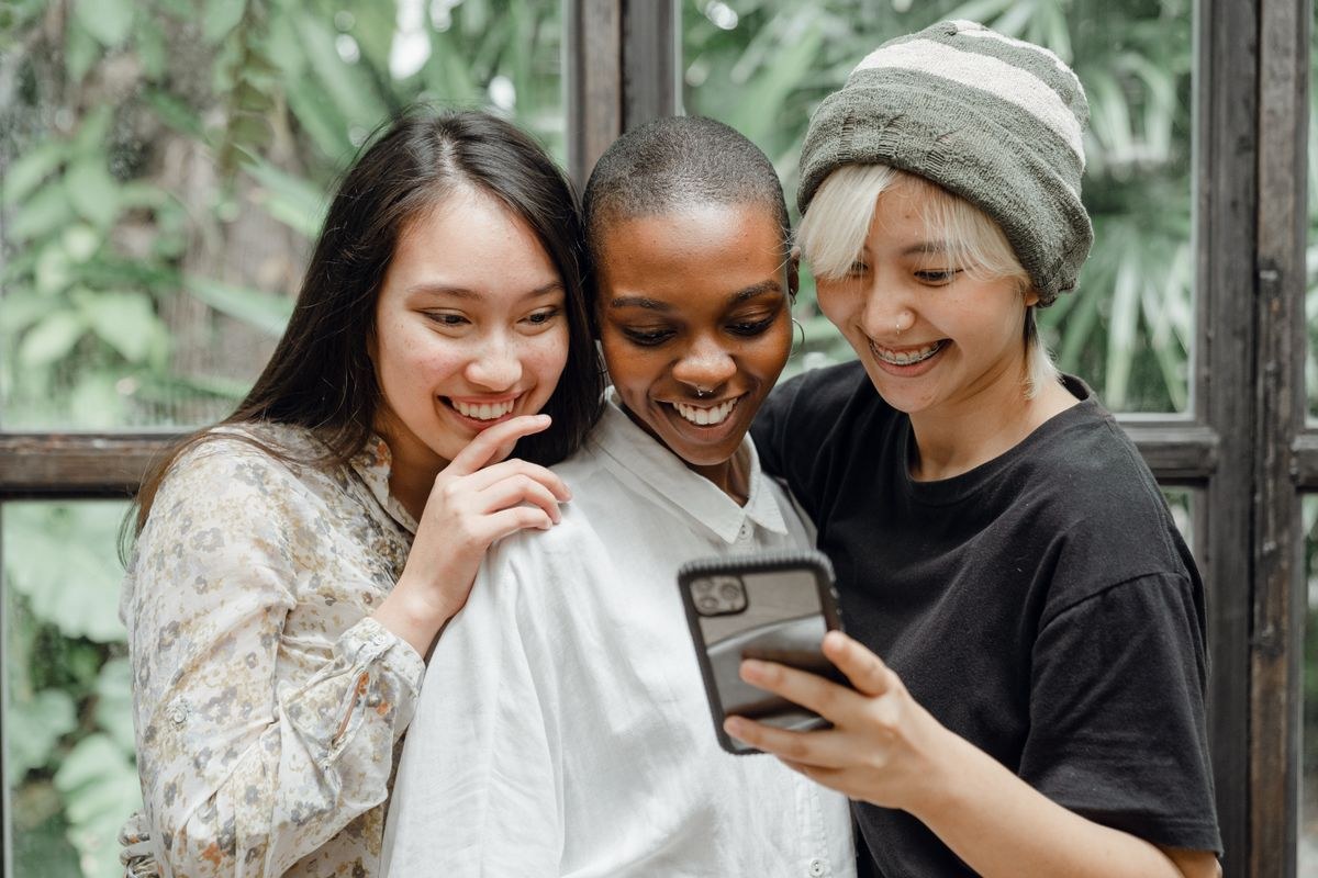 Three friends laughing together while looking at a phone